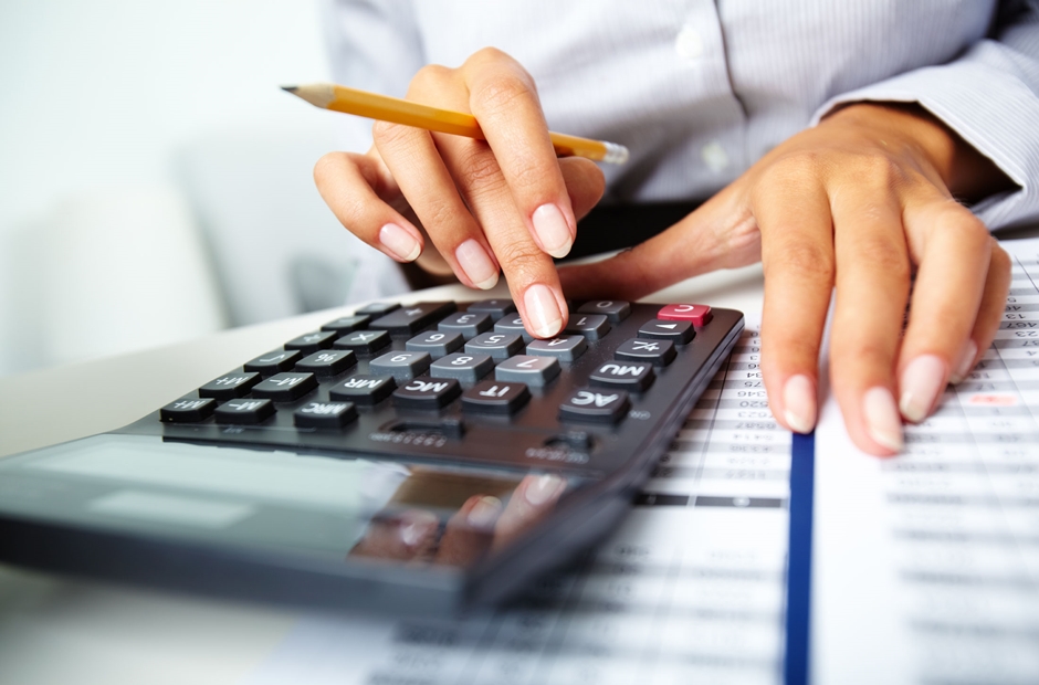 Mão feminina usando camisa clara fazendo contas na calculadora, ilustrando abono de permanência cálculo de benefícios.
